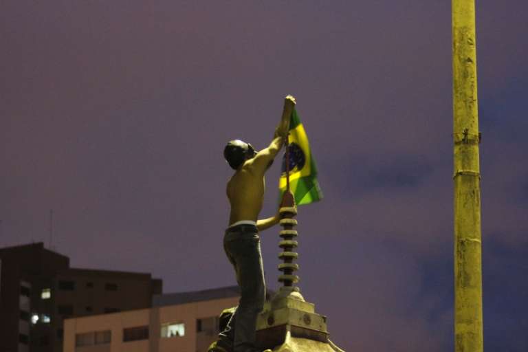 Manifestante coloca a bandeira do Brasil em monumento na Praça do Rádio. (Foto: João Garrigó)