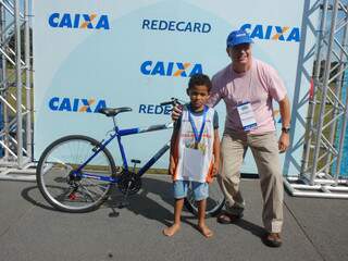 Cleber recebe bicicleta do superintendente da Caixa Econômica em MS, Paulo Antunes Siqueira. (Foto: Simão Nogueira)