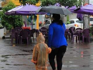 Mãe e filho tentando se proteger da chuva no Centro de Campo Grande nesta manhã (Foto: Marina Pacheco)