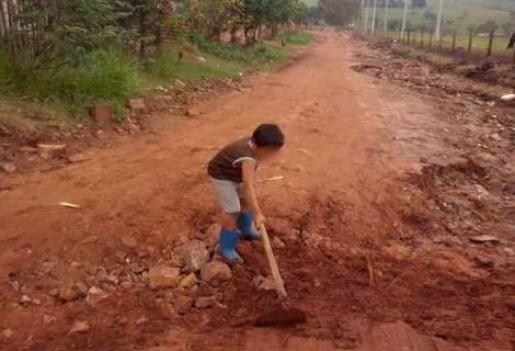 Com enxada na mão, criança é vista tapando buraco de rua de terra 