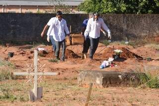 Funcionários retiram caixão de cova no Cemitério Cruzeiro (Foto: Marcelo Victor)