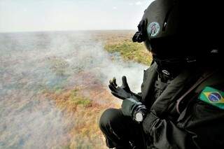 Militar vendo foco de incêndio de cima, de dentro do helicóptero (Foto: Saul Schramm/Governo do Estado)