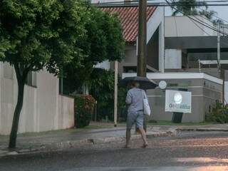 Pedestre se protege da chuvinha fraca por volta das 6h em rua do Jardim dos Estados, em Campo Grande (Foto: Henrique Kawaminami)