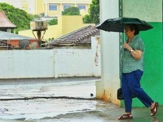 Senhora se protege de chuva no centro de Campo Grande (Foto: André Bittar)