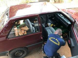 Policial retirando os tabletes da droga dos fundos falsos do veículo. (Foto: Divulgação/PMR) 