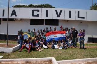 Delegado, de camisa preta, junto com as crianças em frente à delegacia, que fica a 40 metros do Paraguai. (Foto: reprodução Facebook)
