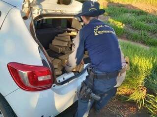 Policial contando os tabletes de maconha encontrados no veículo. (Foto: Divulgação/PMR) 