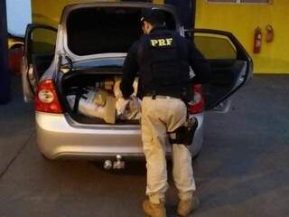 Policial contando os tabletes de maconha encontrados no veículo. (Foto: Divulgação/PRF) 
