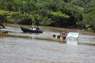 Pessoas são transportadas em barcos, placa de trânsito mostra nível da água. (Foto: Almir Portela)