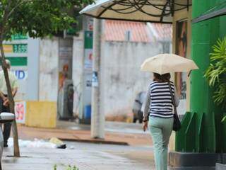 Mulher prevenida com guarda-chuva andando por rua de Campo Grande hoje (Foto: André Bittar)