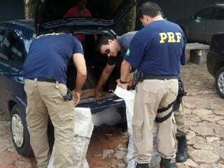 Policiais recolhendo a droga que estava no porta-malas do veículo (Foto: divulgação PRF)