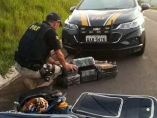 Policial revistando as duas malas do suspeito, onde estavam os tabletes da droga. (Foto: Divulgação/PRF) 