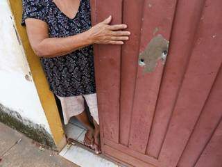 Idosa apontado para marcas de tiros no portão da residência (Foto: Paulo Francis)