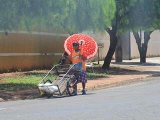 Trabalhador com guarda-chuva para se proteger do sol quente (Foto: Marina Pacheco)