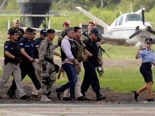 Jarvis Gimenes Pavão é conduzido por policiais paraguaios e brasileiros minutos antes de ser extraditado para o Brasil, na quinta (Foto: Reuters)