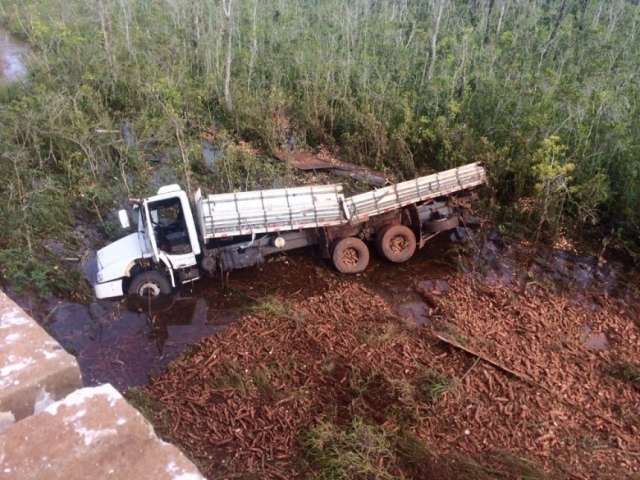 Carregado com 18 t de mandioca, caminh&atilde;o cai em c&oacute;rrego na MS-276