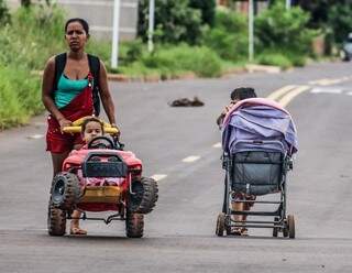 Criança empurrando carrinho do irmão ao lado da mãe que também levava outro filho para passear (Foto: Marcos Maluf)