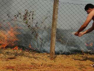 Ezequias tenta apagar o fogo na cerca do quintal da casa dele jogando água (Fotos: Rodrigo Pazinato)