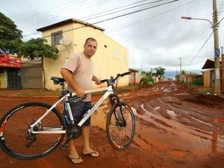 Edson Alves enfrenta de bicicleta lama em rua que seria asfaltada no Aero Rancho (Foto: André Bittar)
