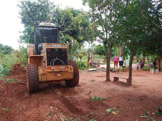 Moradores assistem máquina destruir plantação em terreno.