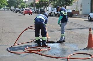 Funcionários limpando os tampões do esgoto que ficam na rua. (Foto: Marcelo Calazans)