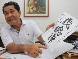 Seiki mostra alguns escritos que fez, em papel, para a Associação Okinawa. Para chegar no resultado, ele precisou escrever cerca de 25 vezes. (foto: Marina Pacheco)