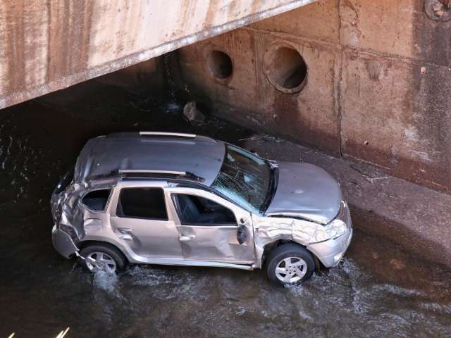 Carro bate em meio-fio, cai em c&oacute;rrego e motorista fica ferido 