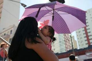 Mulher e sua filha assistindo ao desfile de aniversário da cidade protegidas com uma sombrinha (Foto: João Paulo Gonçalves)