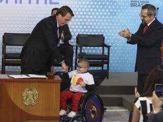 Presidente  assinou medida com a presença de estudante cadeirante. Ao lado, o ministro da Educação aplaude a cena. (Foto: Agência Brasil)