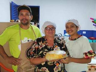 Dona Diodete no centro, segurando um bolo pronto embalado para venda, do seu lado os ajudantes (Foto: Arquivo pessoal)