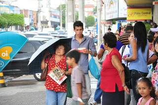 Senhora se protege com guarda chuva, no Centro de Campo Grande.