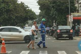 A cena interrompe a hostilidade: trabalhador ajuda idosa a atravessar a rua (Foto: Henrique Kawaminami)