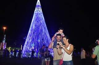 Camila e a família olhavam as fotos tiradas com a árvore de Natal de fundo, nas cores azul e branca.