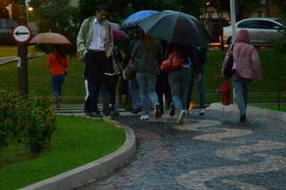 Chuva obriga trabalhadores a se protegrem com guarda-chuva. 