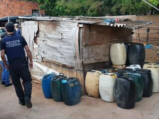 Policial federal ao lado de tambores de plástico onde combustível ilegal era estocado (Foto: Divulgação/PMA)