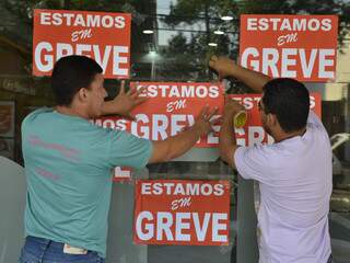 Membros do sindicato colam cartazes informando sobre em agências bancárias da região central de Campo Grande. (Foto: Minamar Júnior)