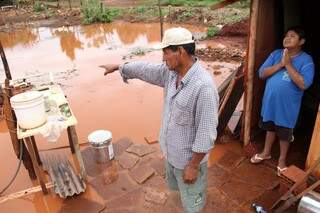 Morador mostra para água que invadiu seu barraco em assentamento, enquanto filho pede a Deus que não chova novamente. (Foto: Marcos Ermínio)