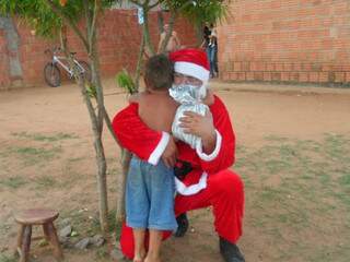 Papai Noel abraça menino antes de entregar presente.