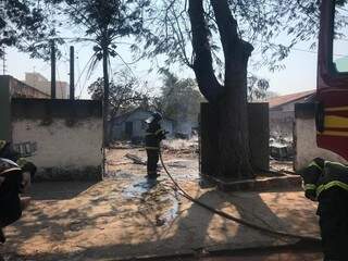 Bombeiros trabalhando no rescaldo do combate às chamas; nos fundos, a outra casa de madeira construída no terreno (Foto: Danielle Matos)