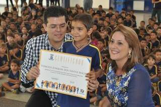 O prefeito e a primeira-dama Andrea Olarte entregam certificado ao aluno Vinícius, número 100 mil da rede municipal. (Foto:Marcelo Calazans) 
