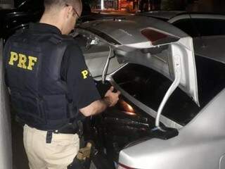 Policial quantificando a droga que estava no porta malas do veículo. (Foto: Divulgação/PRF) 
