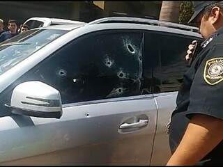 Policial paraguaio observa buracos de bala no vidro da Mercedes de Gustavo Alvarenga (Foto: Direto das Ruas)