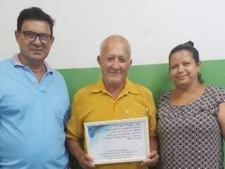 Raimundo (ao centro) entrega placa para Mauricéia (à esquerda): agradecimento e respeito ao professor. 