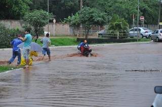 Motociclista cai ao tentar atravessar via alagada pelo Córrego Segredo (Foto: Marcelo Calazans)
