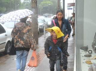 Garoto se protege da garoa fina com toalha na cabeça, no centro de Campo Grande. (Foto: Minamar Junior)