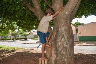 Edson em cima de um caixote tentando subir na árvore. (Foto: Alana Portela)