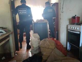 Policiais em um dos cômodos do imóvel ao lado dos tabletes de maconha. (Foto: Divulgação/PM) 