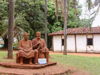 Escultura de Luiz, a esposa e a filha. Ao fundo, a casa de pau-a-pique. (Foto: Henrique Kawaminami)