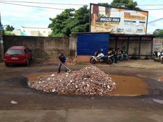 Buraco no Bairro Tiradentes sendo tampado por funcionário da farmácia em frente (Foto: Direto das ruas)