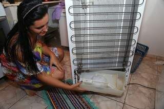 Bianca Figueiredo mostra recipiente com água acumulada atrás da geladeira. (Foto:Fernando Antunes)